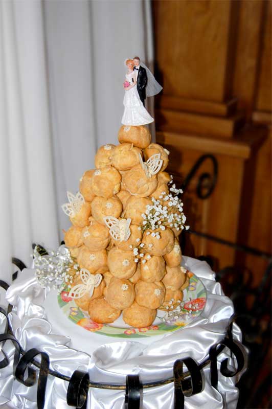 Конусоподібний весільний торт з еклірів з фігурками молодят зверху.