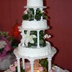 Триярусний білий весільний торт з фонтаном у середині та фігурками молодят зверху.