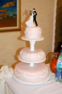 Триярусний блідо-рожевий весільний торт з фігурками молодят зверху.